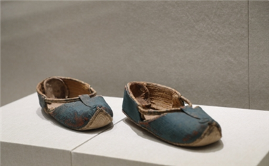 △ 唐·蓝色如意鞋，1968年吐鲁番阿斯塔那104号墓出土，新疆维吾尔自治区博物馆藏。鞋面为蓝丝绢质，鞋底为白色，鞋头微微翘起，鞋帮至鞋上部用棉条搭缝两条绳，既牢固鞋面，又起到装饰作用。该鞋形制类似今天的凉鞋，适合夏季穿着。